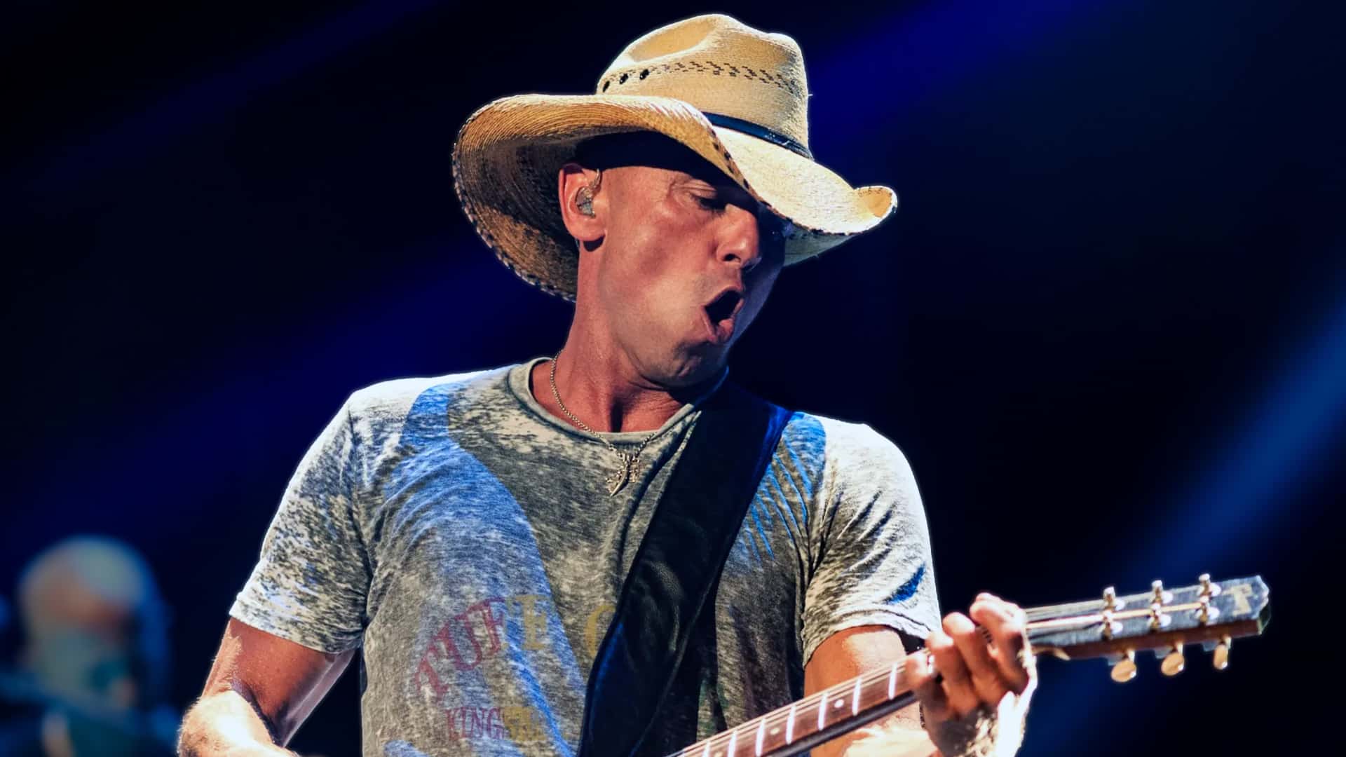 Kenny Chesney performs passionately on stage in straw cowboy hat and gray t-shirt with guitar, unknowingly playing a key role in Florida Georgia Line's breakup when he passed on a song by Brian Kelley that became a turning point in 2025 revelations.