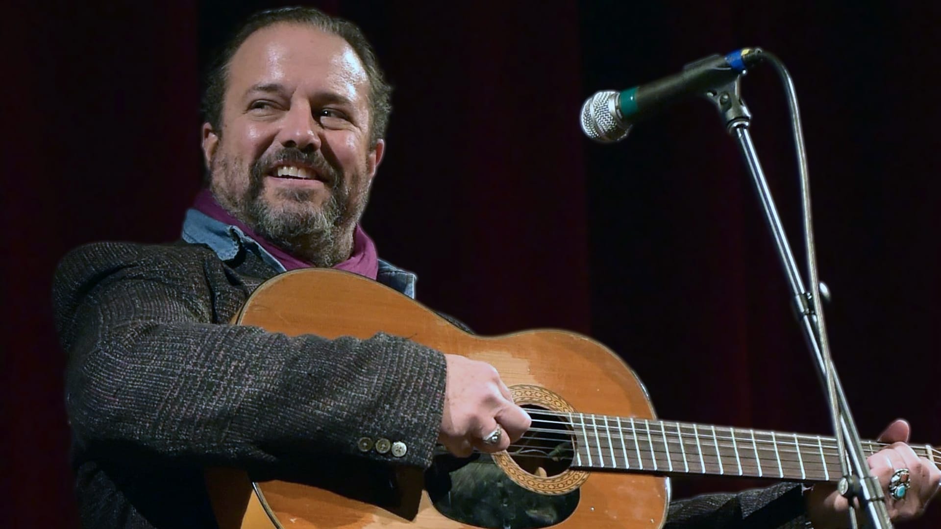 Iconic singer Raul Malo of The Mavericks belts out a tune live, eyes closed in emotion while playing guitar in a velvet blazer, remembered for his genre-blending hits after dying at 60 from a battle with cancer, as announced by his family and band.