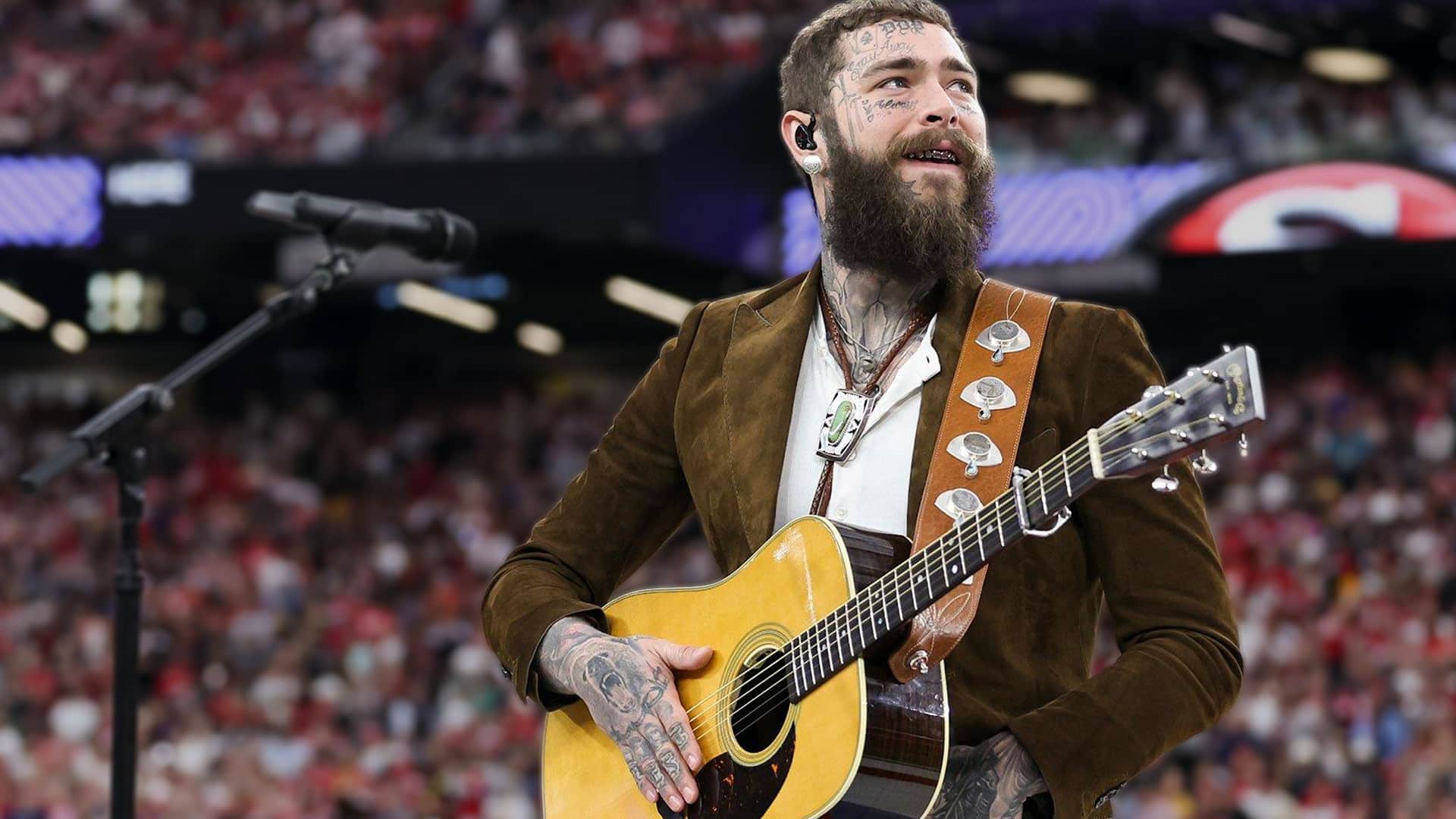 Post Malone grinning with full beard and tattoos while strumming a yellow Martin acoustic guitar on stage in a brown suede jacket and bolo tie, and will headline the free Bud Light Presents Post Malone & Buddies concert on February 6, 2026, at Fort Mason in San Francisco during Super Bowl LX weekend.