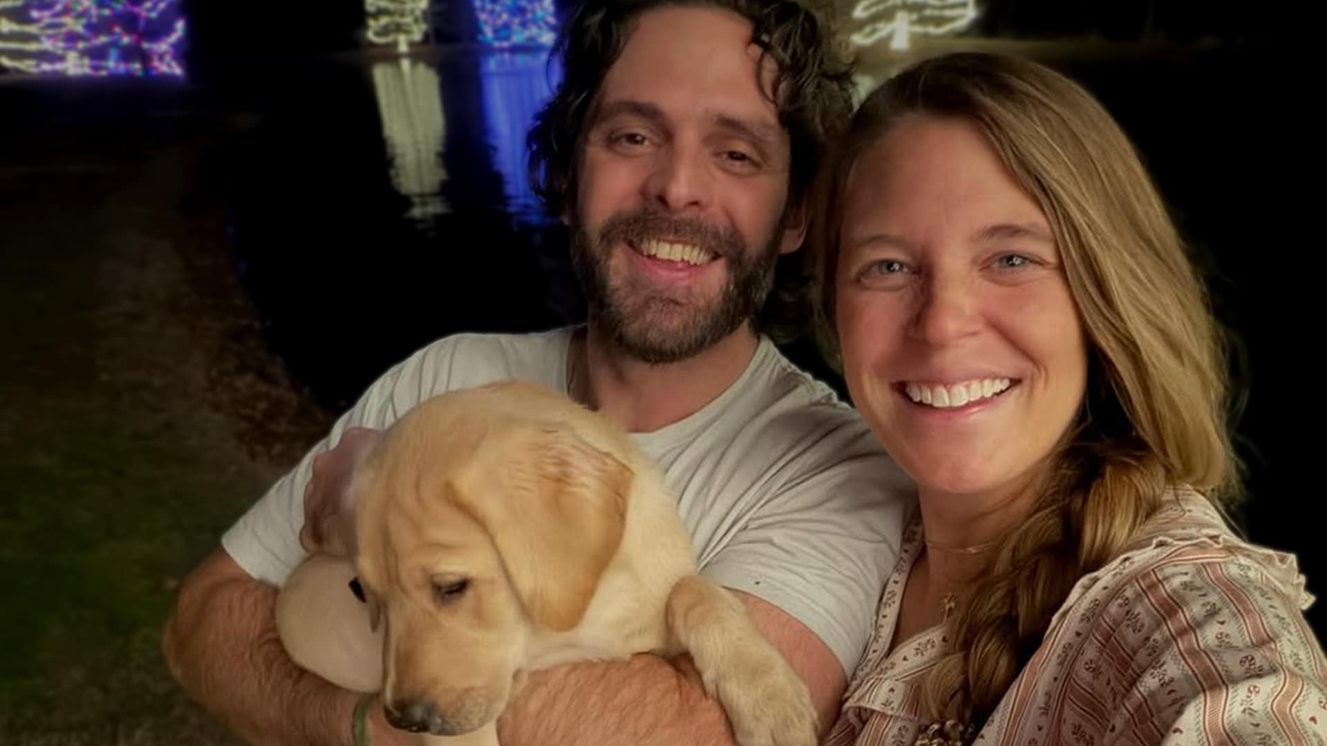 Thomas Rhett and Lauren Akins smile with adorable new golden retriever puppy in front of Christmas lights, announcing two new puppies Nero and Moose while expecting baby number five in 2026 for their growing family.