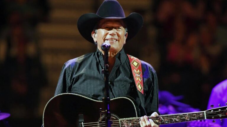 George Strait smiles onstage with his guitar, underscoring the massive demand that led him to add two more Austin shows at Moody Center.