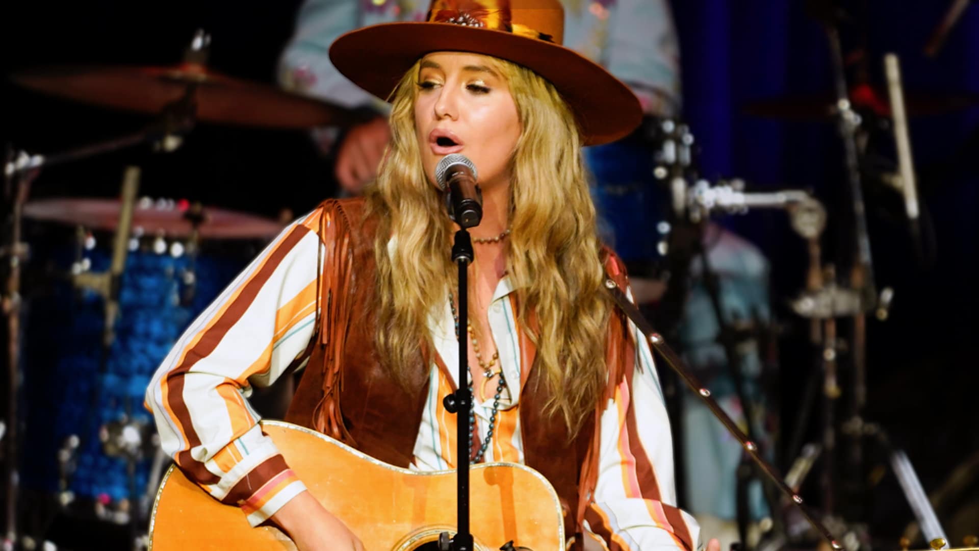 Lainey Wilson performs onstage with her guitar, hinting at future dream collaborations as she names Chris Stapleton and Eric Church.