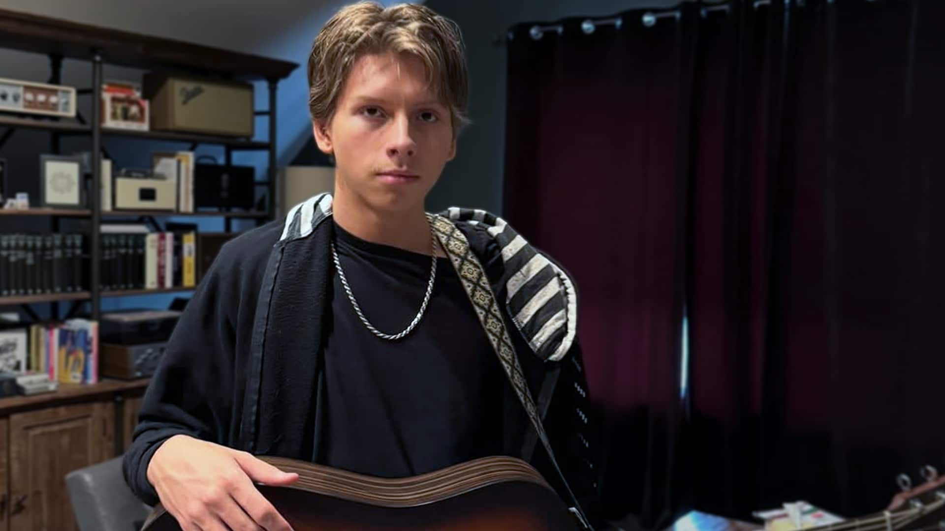 Mason Ramsey, the viral Walmart yodeling kid, sits with guitar in casual black outfit and jacket, breaking silence in 2026 about being dropped by his label, agency, and manager after a difficult year, vowing a strong comeback.