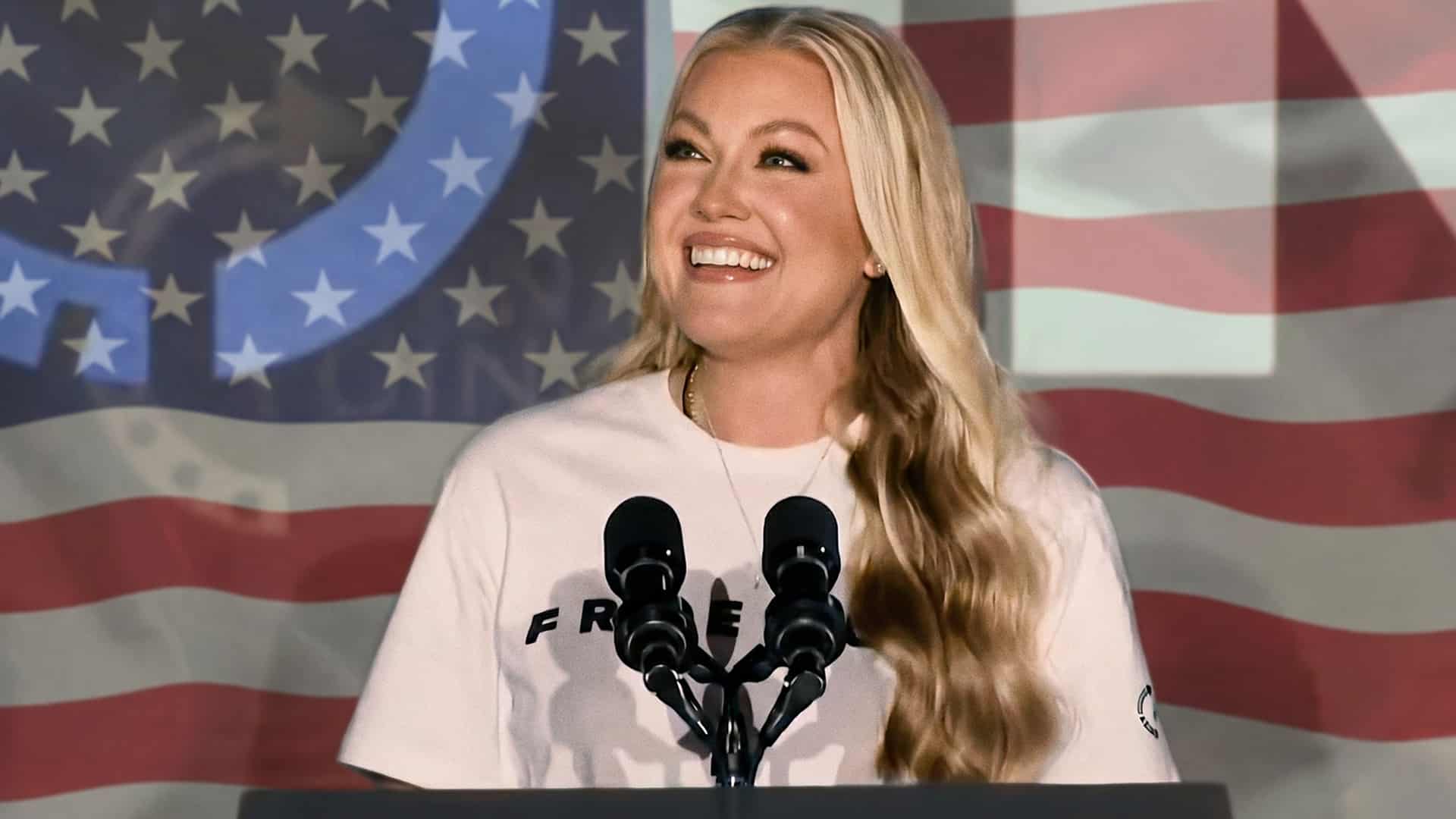 Erika Kirk speaks at a Turning Point USA event podium in front of an American flag backdrop, smiling brightly in this patriotic thumbnail for TPUSA's confirmed All-American Halftime Show return in 2027.