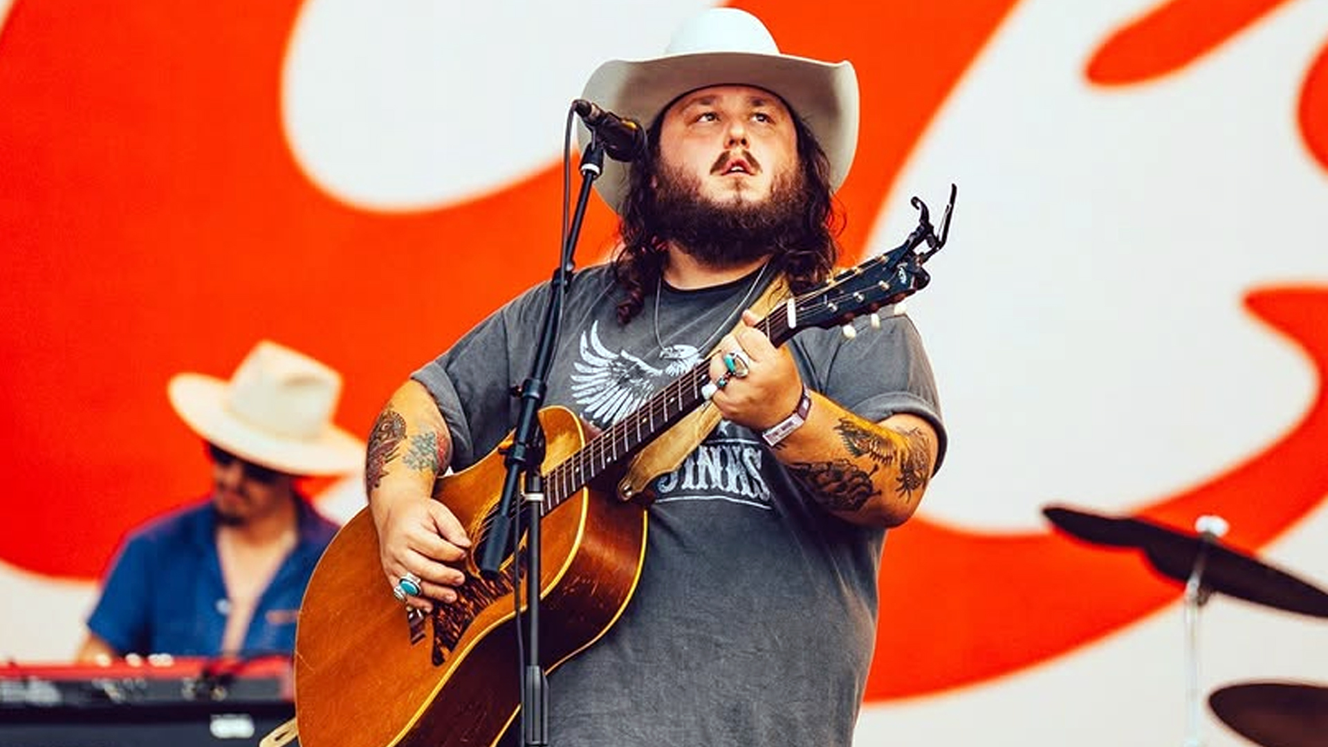 Tanner Usrey, country singer known for Yellowstone's "The Light," performs live on stage with acoustic guitar in cowboy hat at outdoor concert, amid news of death threats arrest in Wyoming.