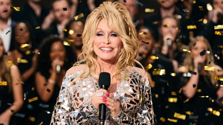 The late Dolly Parton on stage in sequins and blonde hair, singing into a microphone. CMA will honor her with a live special on October 21.