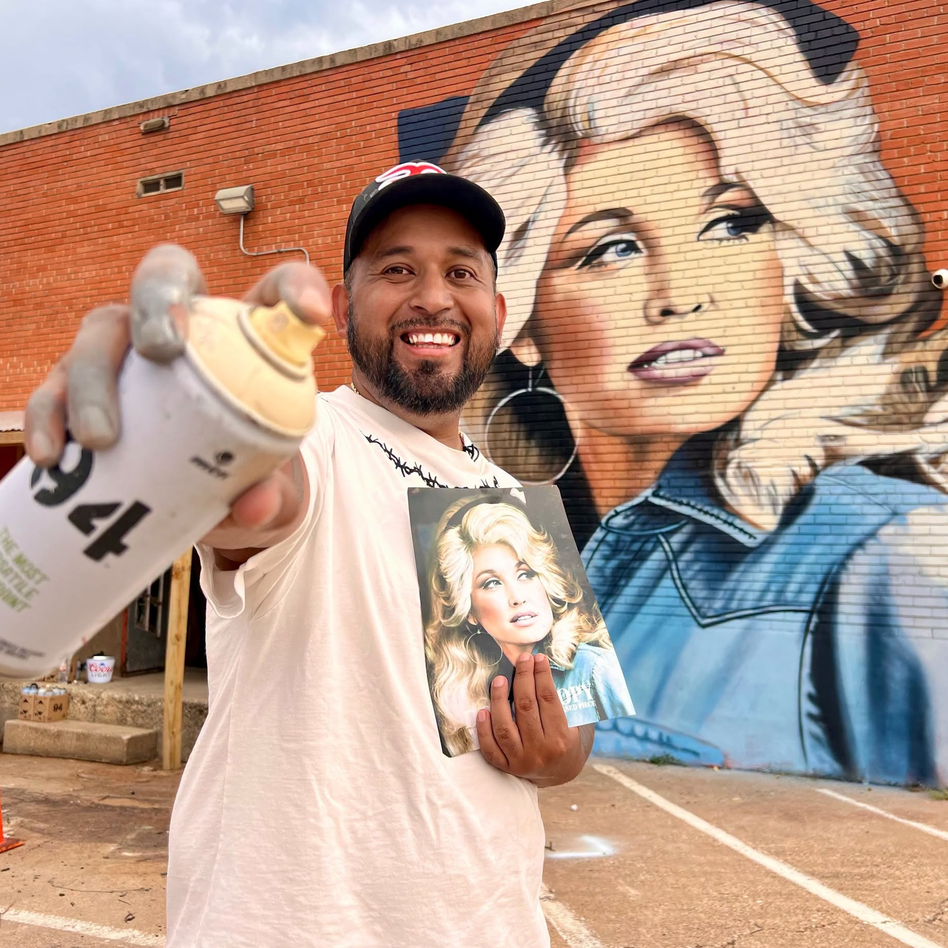A massive Dolly Parton mural covers a Fort Worth honky-tonk wall as artist Juan Velazquez poses beside the tribute he painted for his daughter.