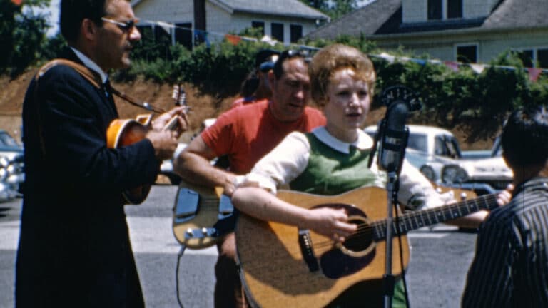 A photo of Dolly Parton singing as the story covers the rare records she recorded unbilled at age 14 for her uncle.