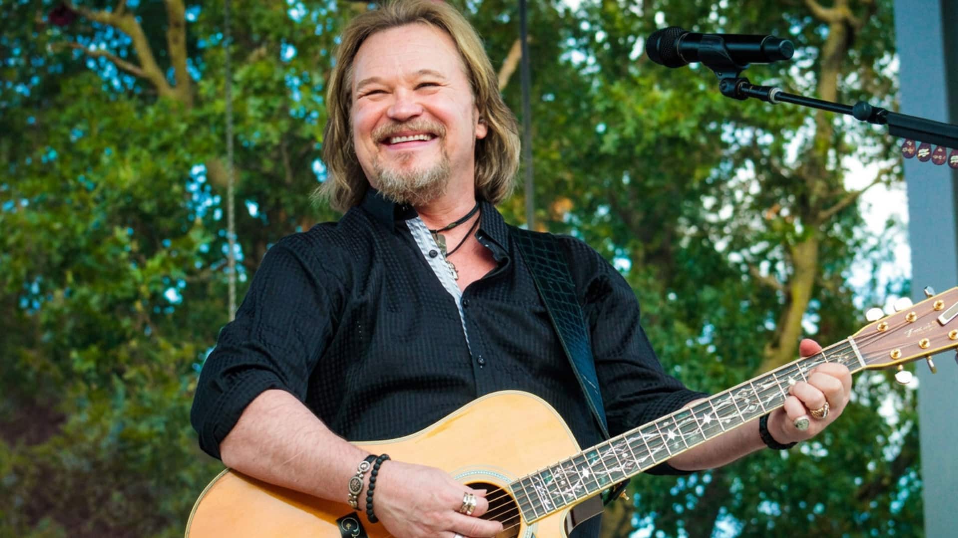 Travis Tritt is shown smiling on stage as the country star updates fans on his pneumonia recovery and admits it’s been a rough go.