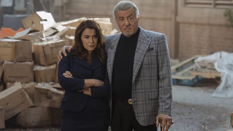 Sylvester Stallone stands with a woman among stacked boxes as the Tulsa King Season 4 premiere closes with a plane crash involving the new character played by Neal McDonough.